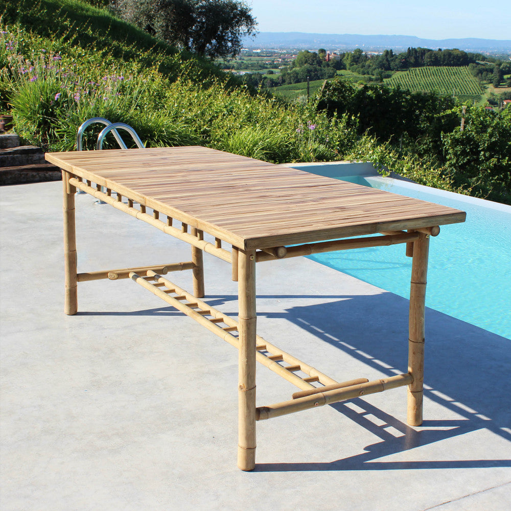 Angolazione laterale del tavolo da giardino in legno Cuba Libre posizionato su un patio in cemento vicino a una piscina.
