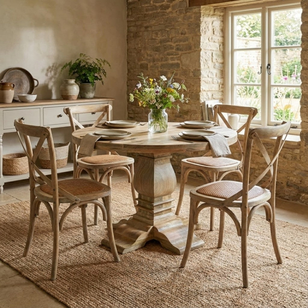 Tavolo rotondo inserito in una sala da pranzo rustica con pareti in pietra e sedie in legno intrecciato.
