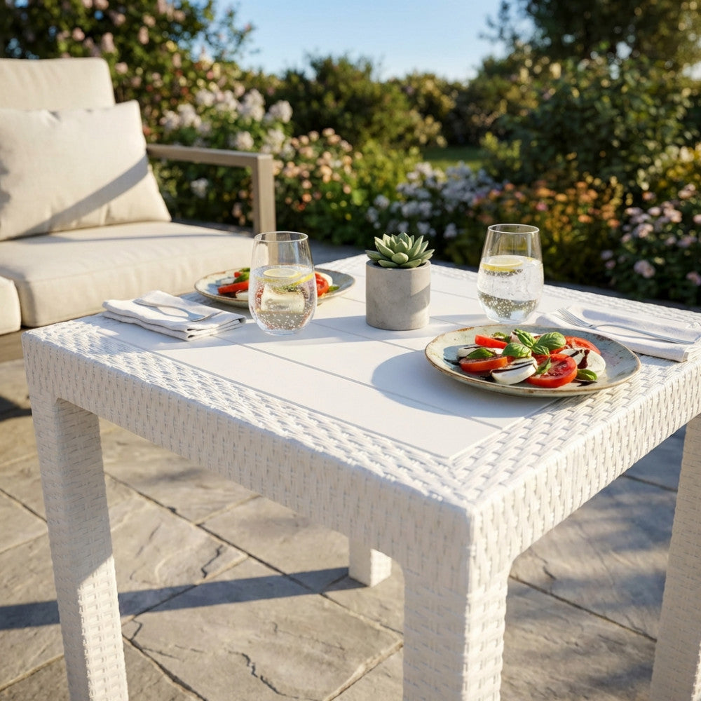 Dettaglio del tavolo Dallas 80x80 in wicker bianco con bicchieri e antipasti all'aperto.
