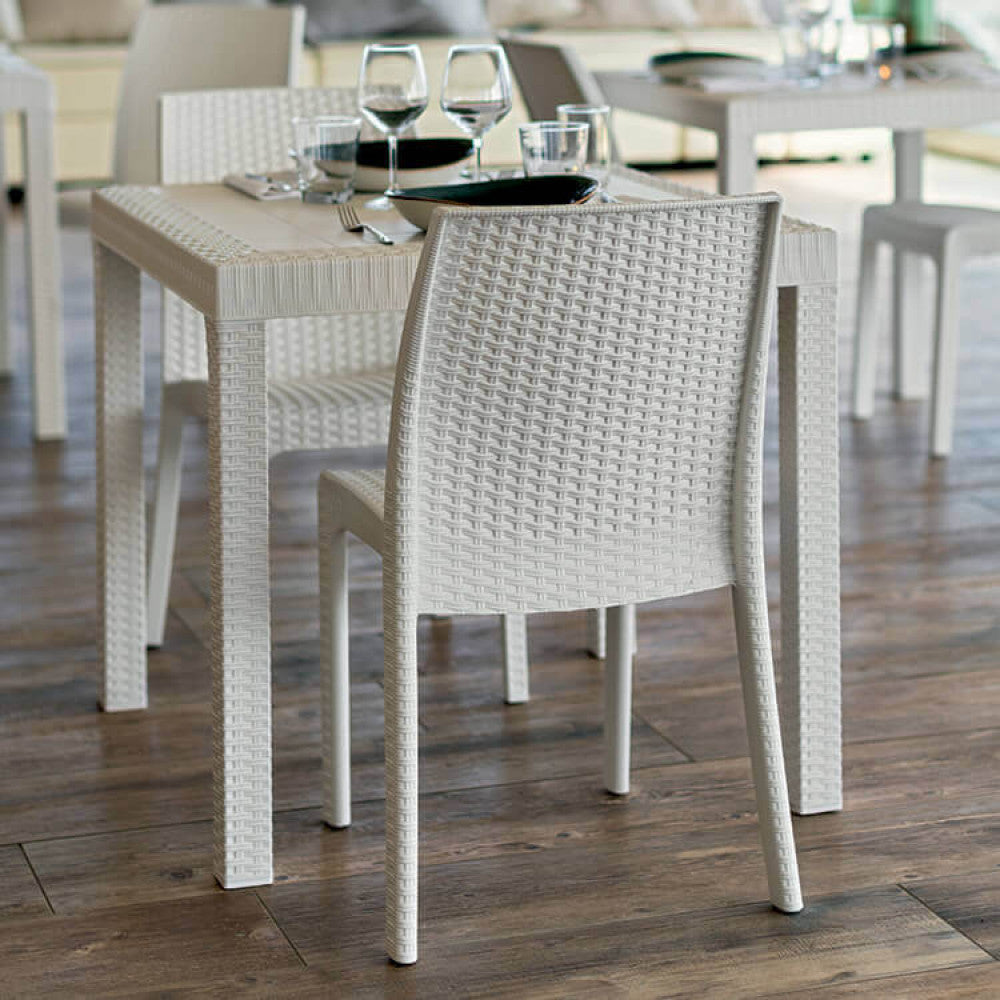 Tavolo Dallas in wicker bianco abbinato a sedie coordinate in un patio pavimentato in legno.