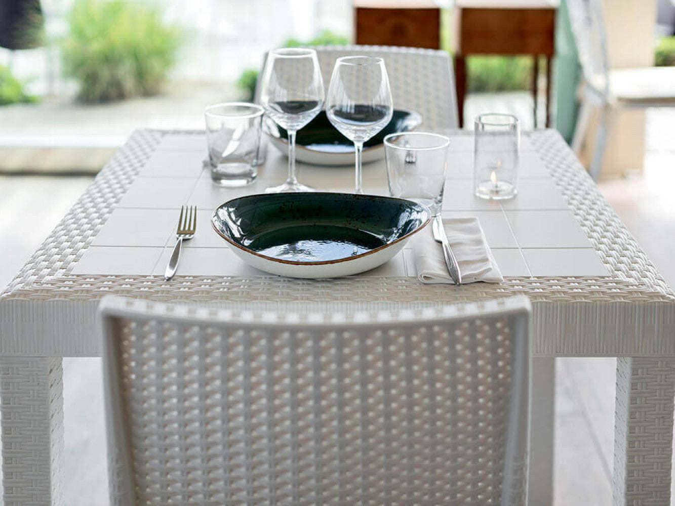 Dettaglio ravvicinato del piano del tavolo Dallas in wicker bianco con piatti in ceramica verde.