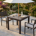Tavolo da giardino Dallas 80x80 in wicker marrone allestito all'aperto con ombrellone centrale e sedute coordinate.
