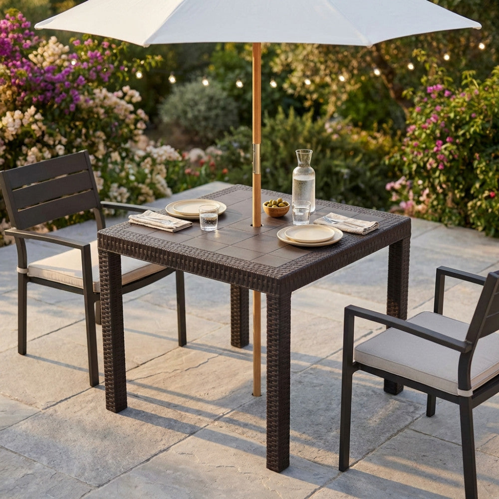 Tavolo da giardino Dallas 80x80 in wicker marrone allestito all'aperto con ombrellone centrale e sedute coordinate.
