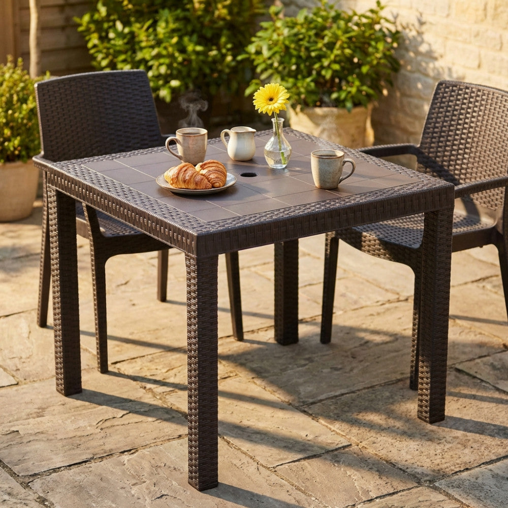 Dettaglio del tavolo da giardino Dallas in wicker marrone con colazione servita su un patio in pietra baciato dal sole.