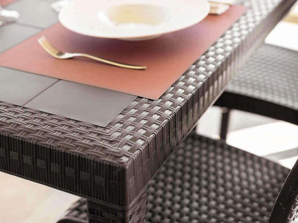 Angolo del tavolo Dallas in wicker marrone allestito con tovaglietta e posate, che esalta il contrasto materico.