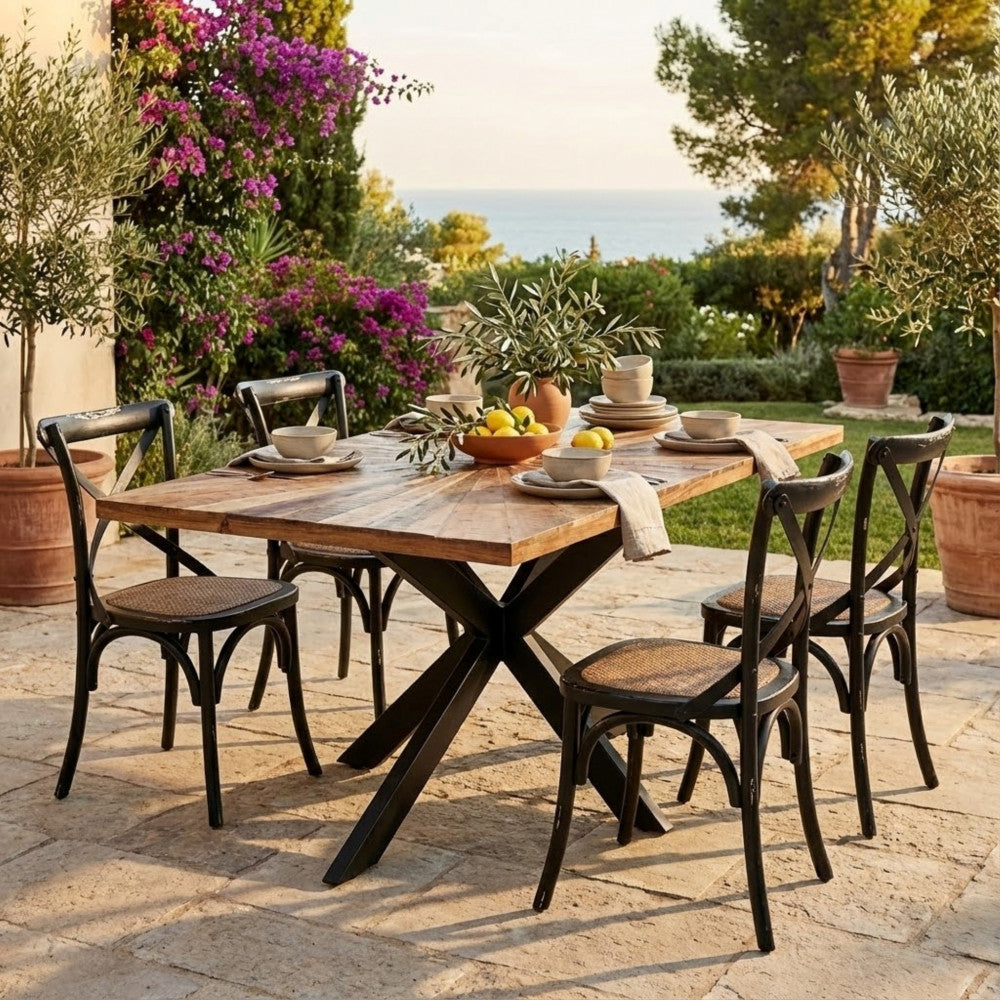Tavolo da pranzo Dannie allestito in un patio esterno soleggiato con sedie nere e vista sul mare.