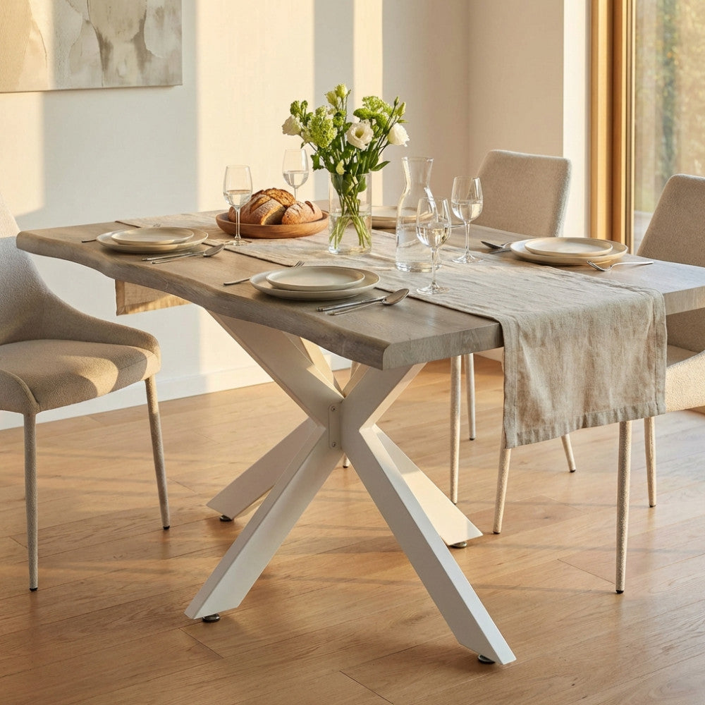 Tavolo da pranzo moderno in melaminico effetto quercia chiaro con struttura bianca a incrocio, allestito in una sala da pranzo luminosa.