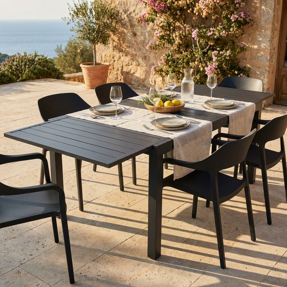 Tavolo da giardino Formentera in alluminio antracite allestito per un pranzo all'aperto su una terrazza in pietra con vista mare.