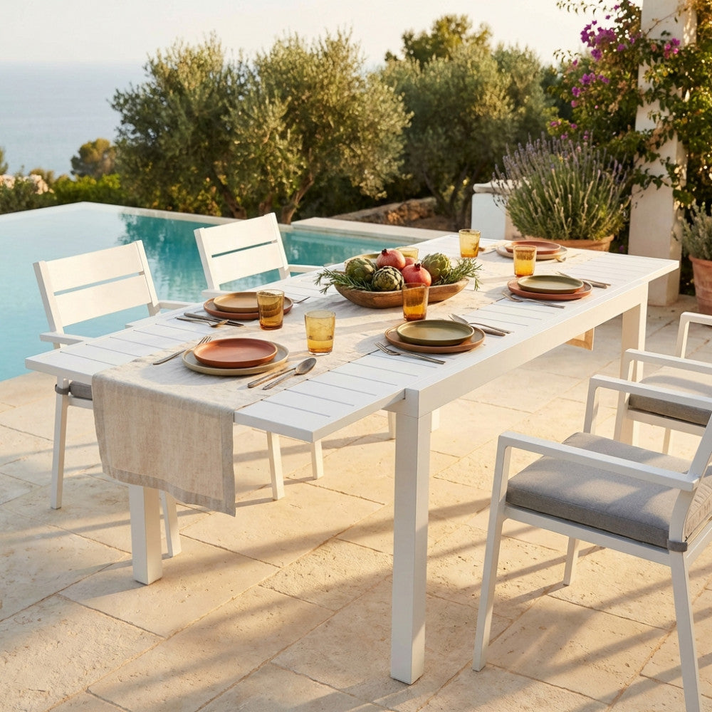 Tavolo da giardino Formentera allungabile in alluminio bianco, allestito per un pranzo a bordo piscina con sedute coordinate.