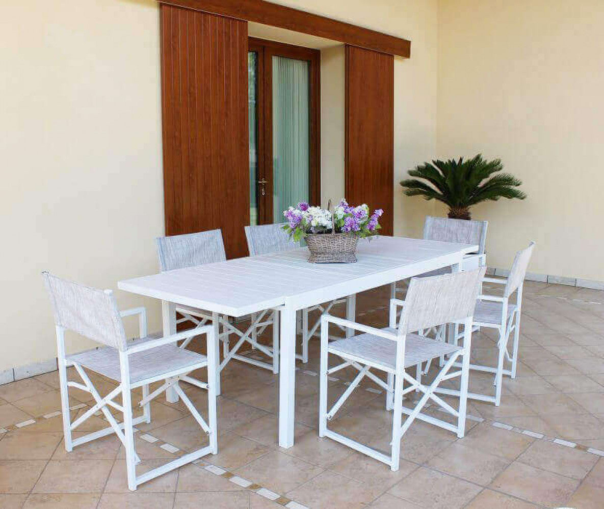 Tavolo Formentera allungato posizionato sotto un porticato elegante, circondato da sedie da regista in tessuto chiaro.