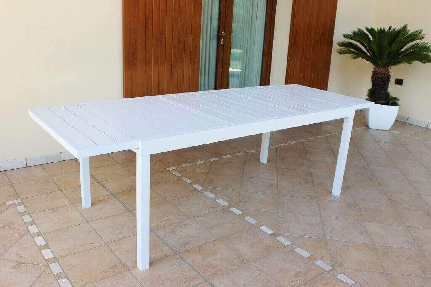 Il tavolo da giardino Formentera in alluminio bianco, mostrato nella sua massima estensione su una pavimentazione in cotto.