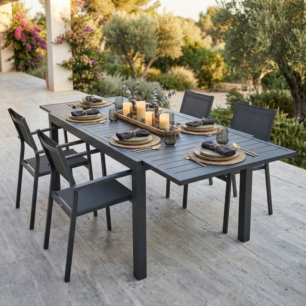 Dettaglio del tavolo allungabile Formentera con centrotavola decorativo e sedute coordinate in un giardino lussureggiante.
