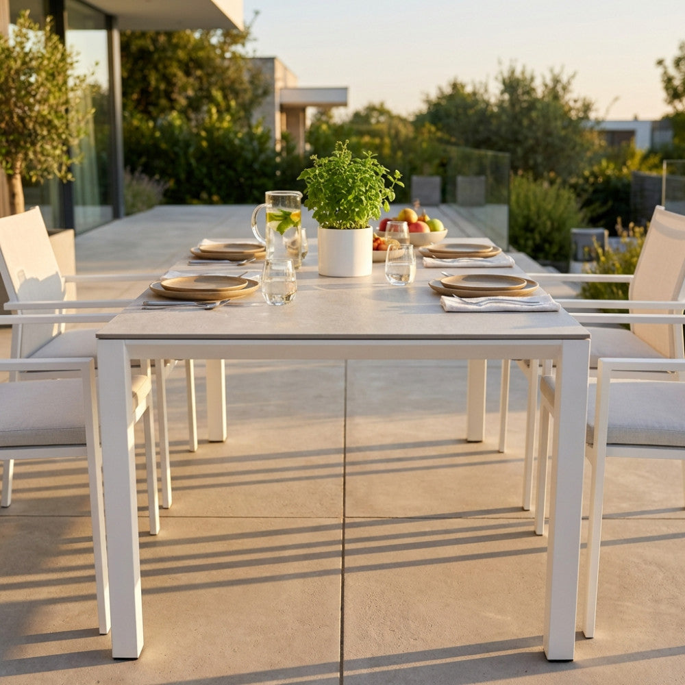 Tavolo da giardino allungabile Freeport in alluminio bianco e pietra sinterizzata, allestito per un pranzo all'aperto su un patio soleggiato.