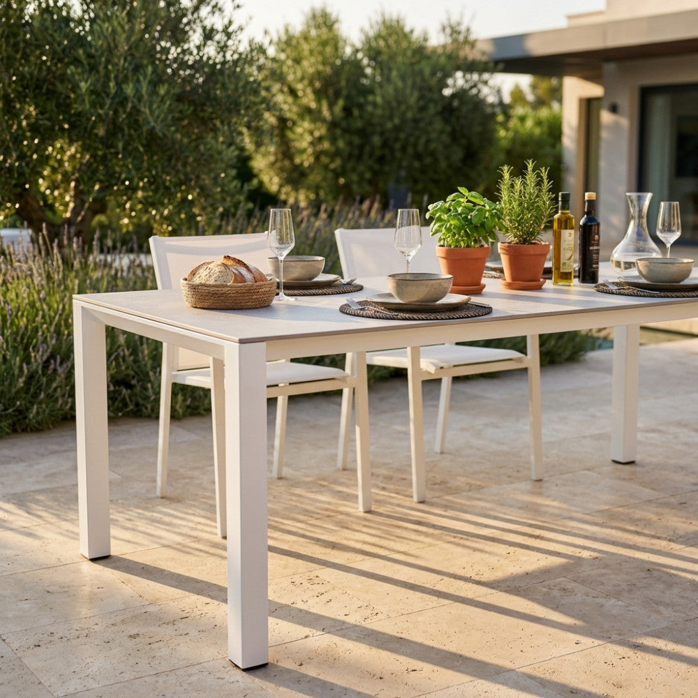 Dettaglio del tavolo da giardino Freeport imbandito con stoviglie in ceramica, calici di vetro e piante aromatiche in vasi di terracotta.