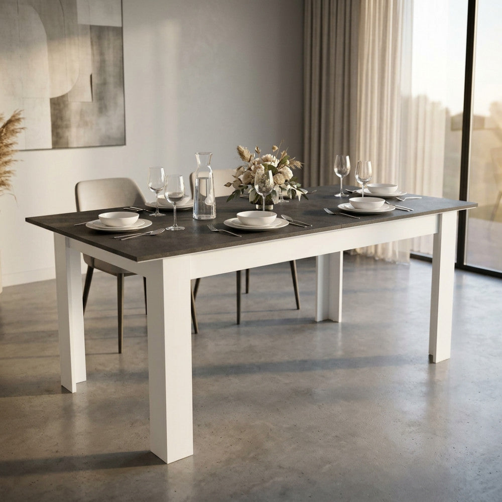 Tavolo da pranzo allungabile Gemma con piano effetto cemento grigio scuro e gambe bianche, allestito in una sala da pranzo moderna e luminosa.