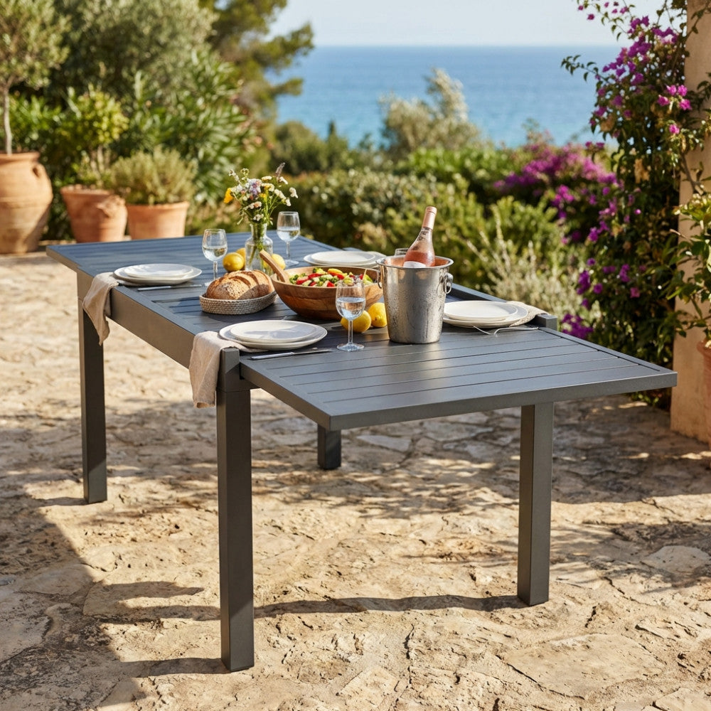 Tavolo da giardino allungabile Hawaii in alluminio antracite allestito per un pranzo all'aperto con vista mare.