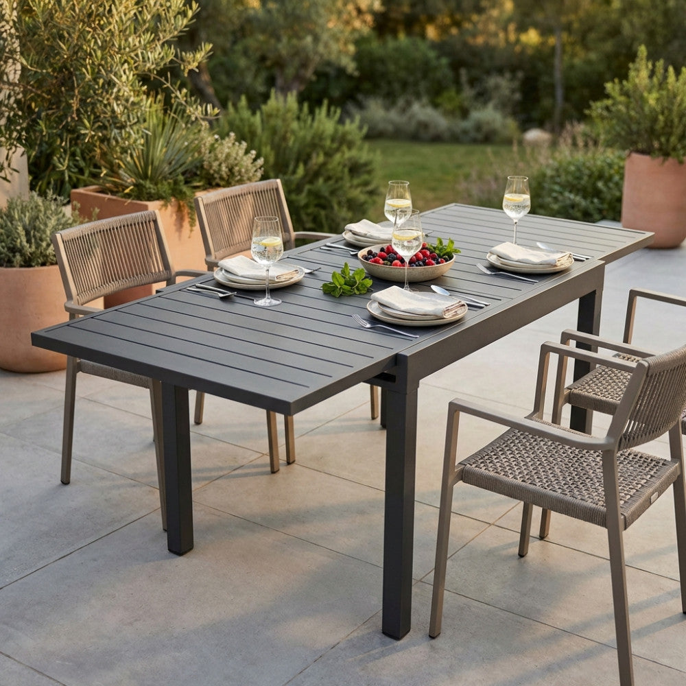 Il tavolo da pranzo allungabile Hawaii in antracite, allestito per un pranzo all'aperto con sei sedie intrecciate su un patio soleggiato.