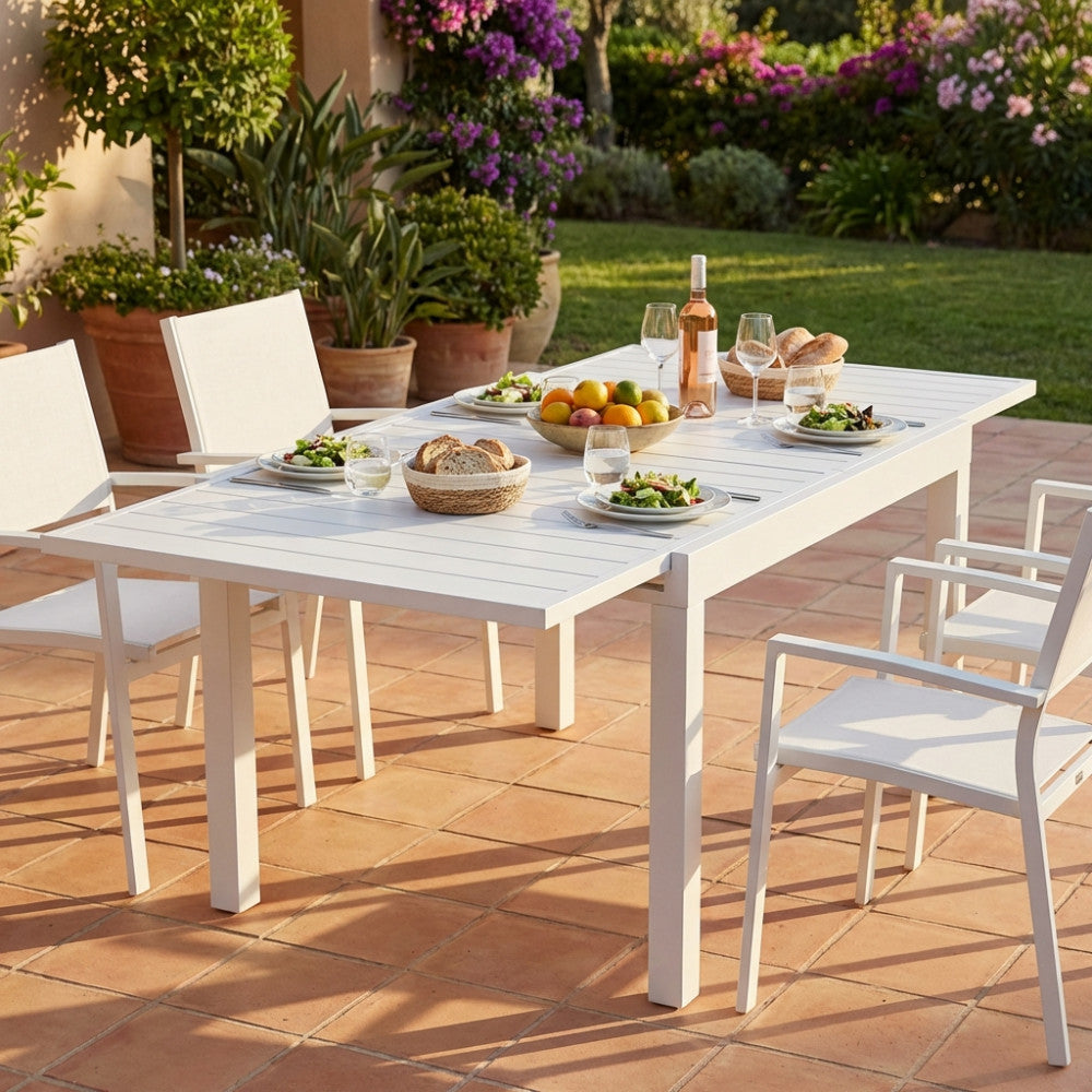Tavolo da pranzo allungabile Hawaii bianco completamente aperto e allestito elegantemente per un pasto all'aperto su una terrazza in cotto soleggiata.