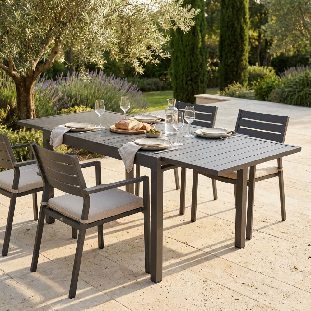 Vista angolare ambientata del tavolo da pranzo allungabile Hawaii in configurazione aperta, caratterizzato da una struttura robusta e un moderno piano a doghe su un patio soleggiato.