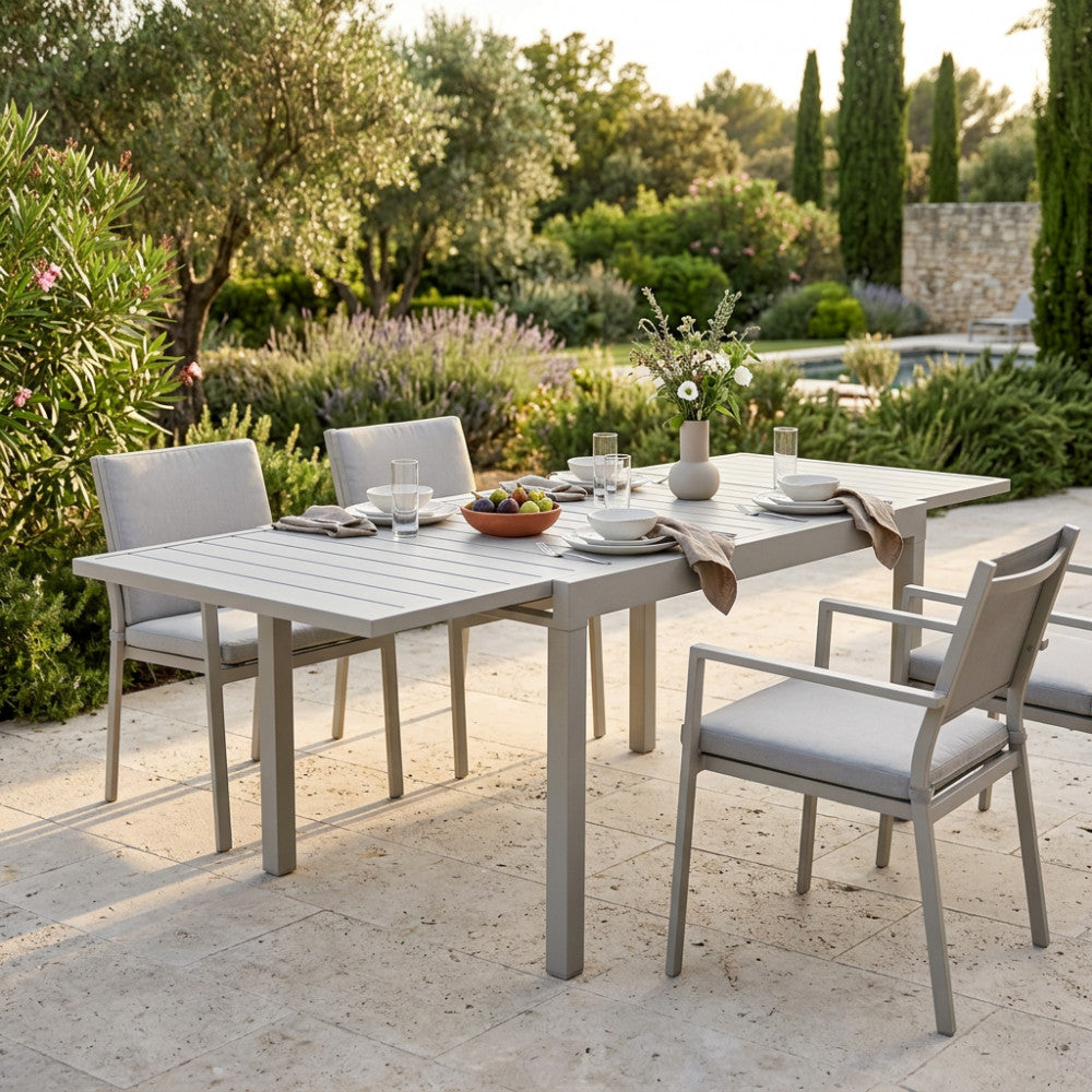 Set da pranzo esterno con tavolo Hawaii allungabile e sedie abbinate in un giardino lussuoso.