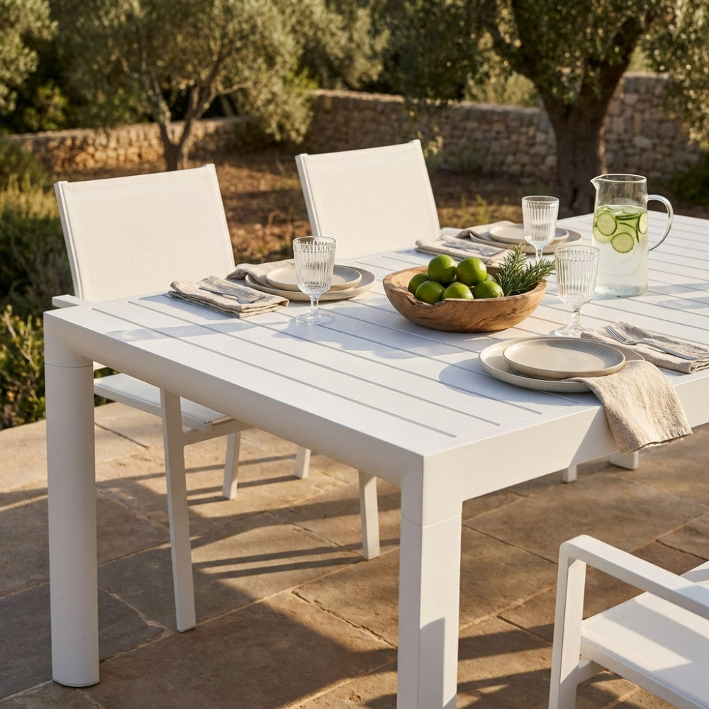 Dettaglio della superficie in alluminio bianco del tavolo Houston con mise en place estiva e luce naturale.
