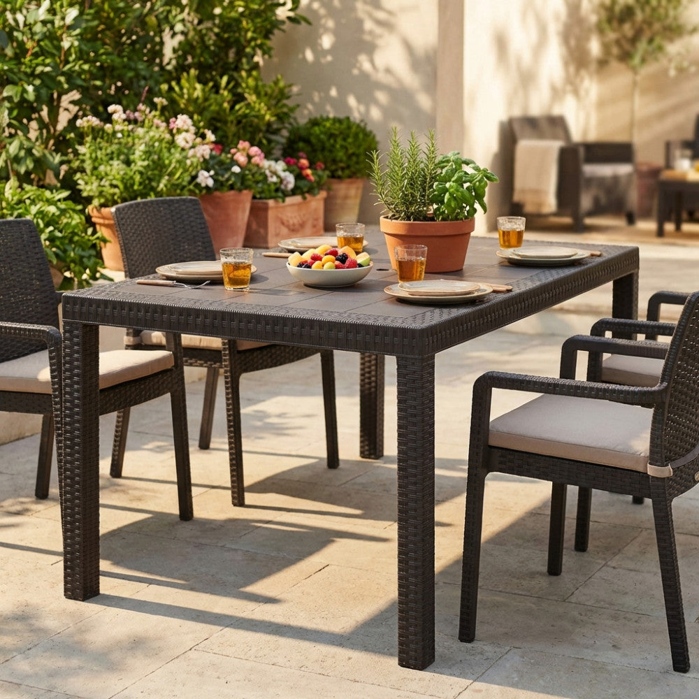 Dettaglio del tavolo da giardino Houston 150x90 in wicker marrone in un patio soleggiato con piante decorative.