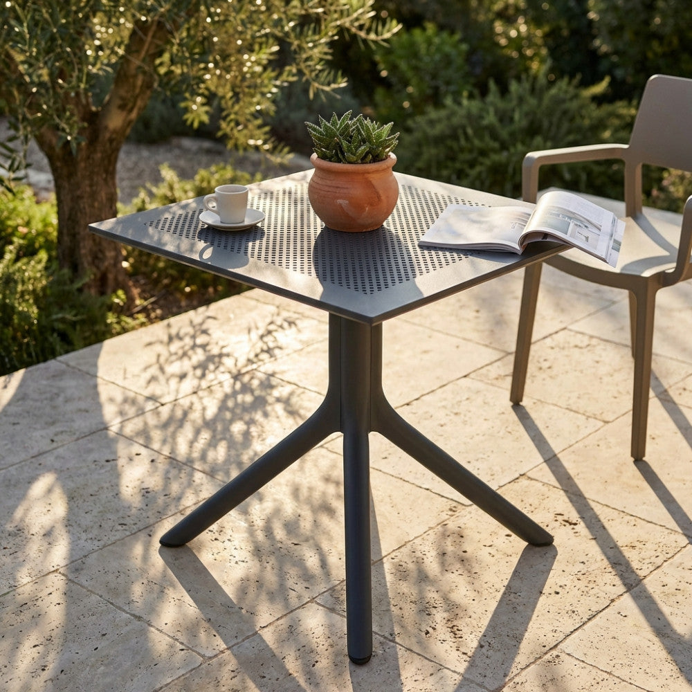 Tavolo da giardino Jarvis 70x70 antracite con piano microforato, allestito su un patio in pietra con pianta e tazzina da caffè.