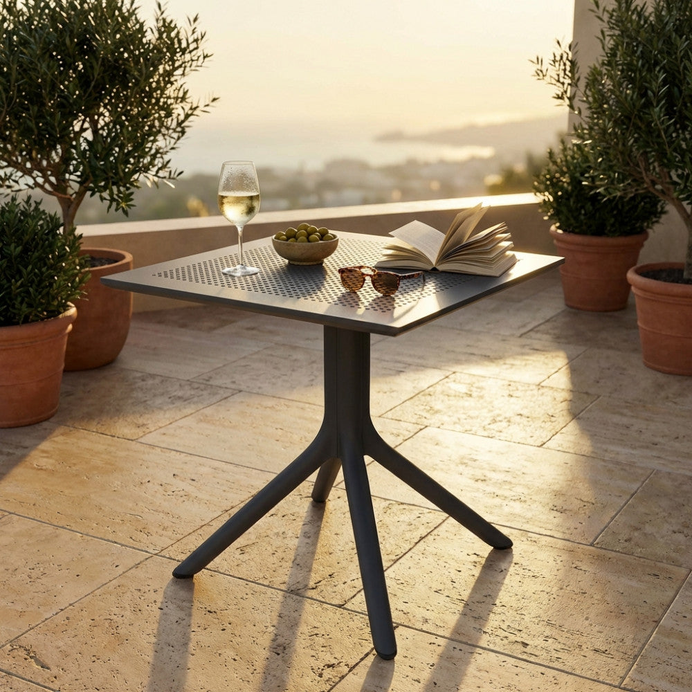 Elegante tavolo da esterno Jarvis al tramonto su una terrazza vista mare, decorato con calice di vino e libro aperto.