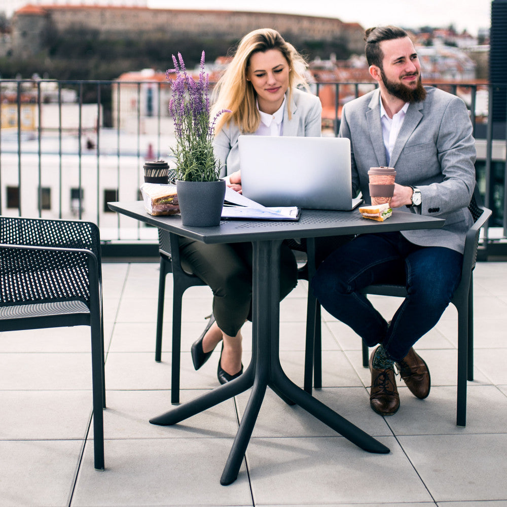 Due professionisti lavorano al computer sul tavolo Jarvis 70x70 in un moderno rooftop urbano, evidenziando la versatilità d'uso.