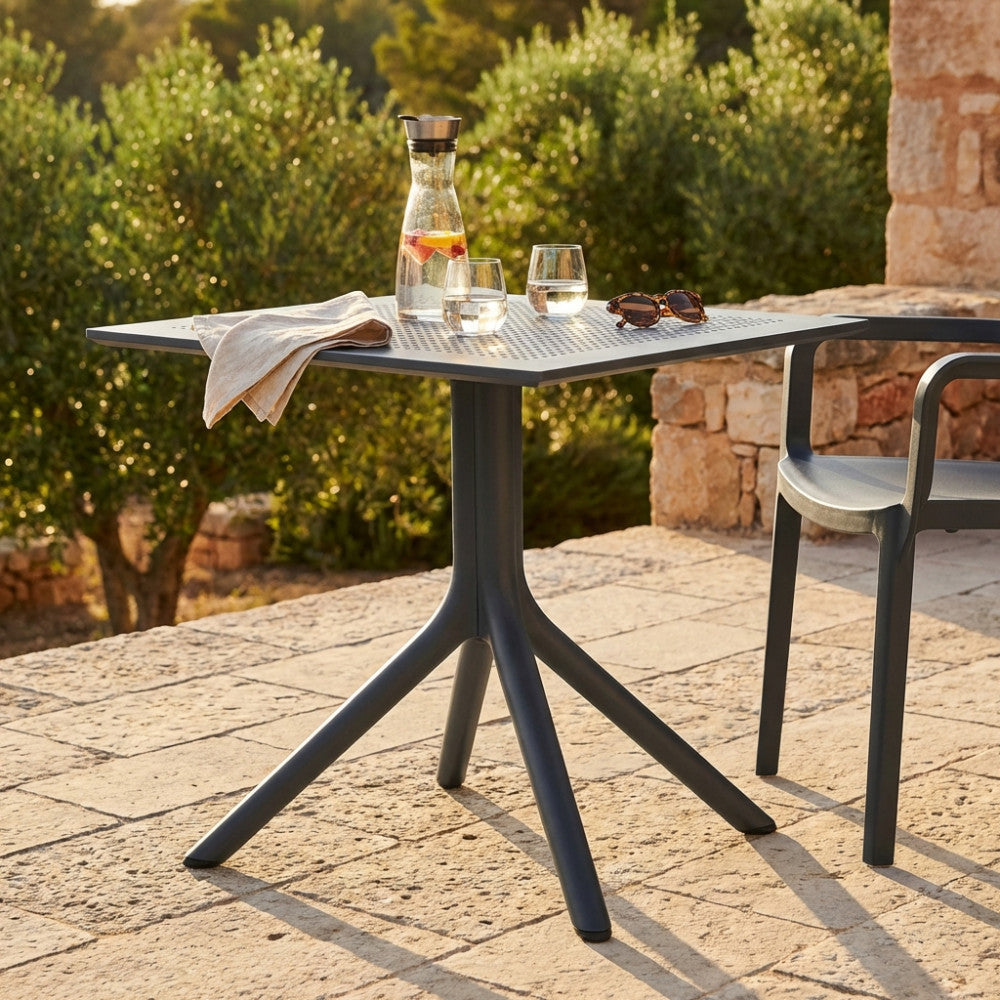 Tavolo da giardino Jarvis antracite allestito con caraffa d'acqua e bicchieri su un patio in pietra illuminato dal sole.