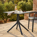 Tavolo da giardino Jarvis antracite allestito con caraffa d'acqua e bicchieri su un patio in pietra illuminato dal sole.