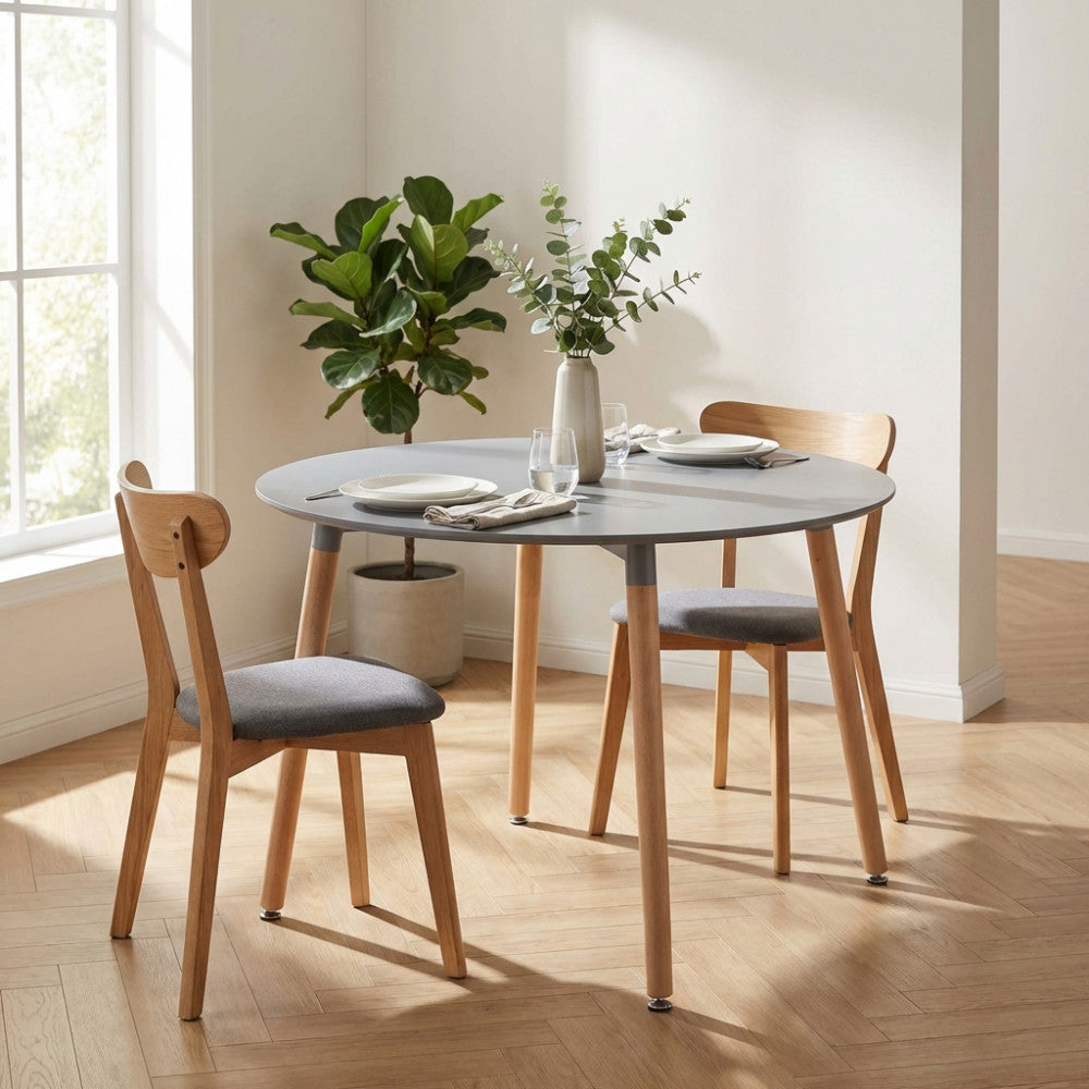 Tavolo Lione rotondo abbinato a sedie in legno e tessuto grigio, decorato con un vaso di eucalipto in un ambiente moderno.
