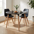 Tavolo da pranzo rotondo nero con gambe in legno, allestito con caffè e croissant, accompagnato da due sedie nere in un ambiente luminoso.