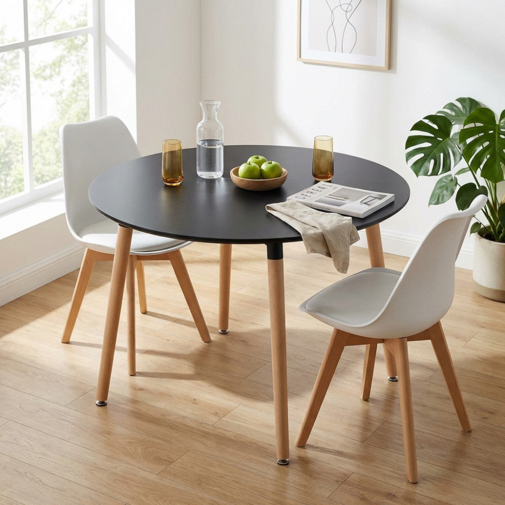 Tavolo rotondo nero dal design moderno, decorato con mele verdi, abbinato a due sedie bianche su un pavimento in parquet.
