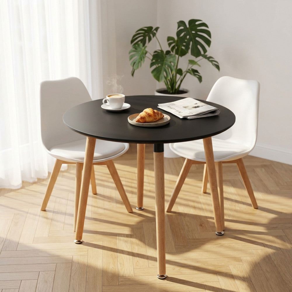 Tavolo da pranzo rotondo nero LIONE con gambe in legno, allestito con colazione in un ambiente luminoso.