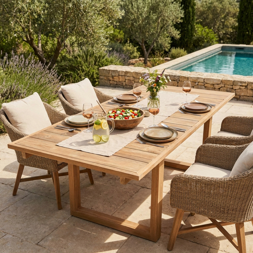 Tavolo da giardino in teak Parker allestito per un pranzo all'aperto con sedute in vimini vicino a una piscina.