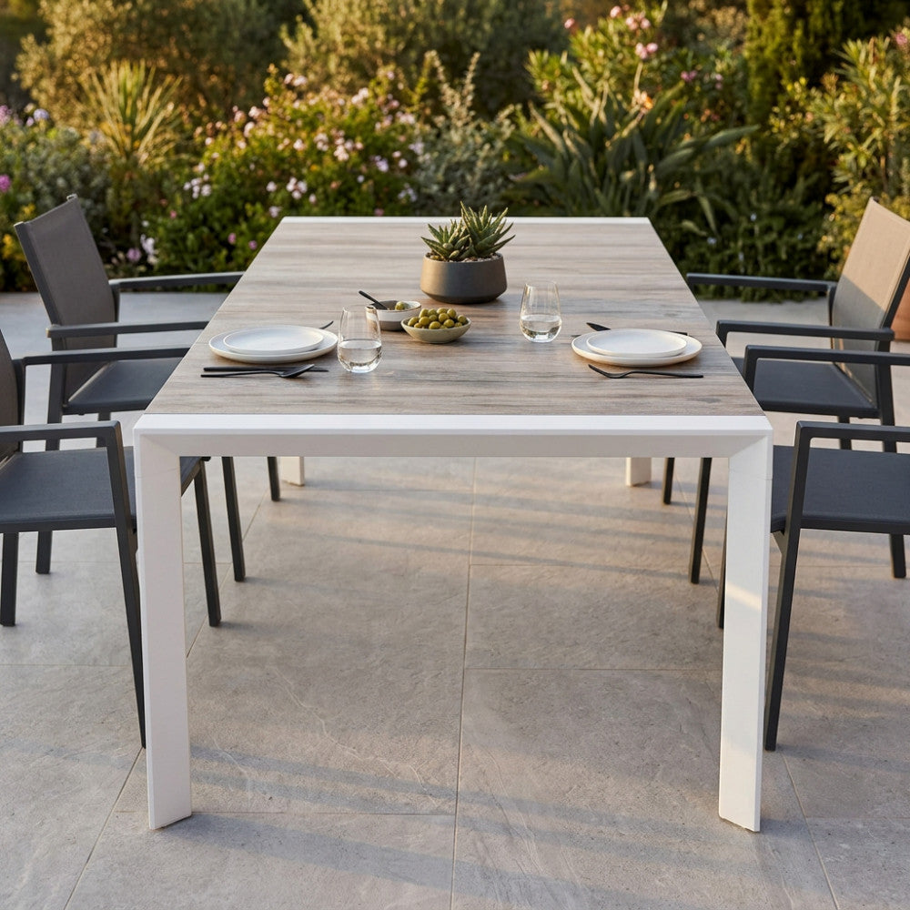 Tavolo da giardino Portland in alluminio e gres allestito su un patio soleggiato con sedie scure moderne.