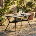 Tavolo da pranzo rettangolare in ceramica allestito con bevande fresche su un patio in pietra illuminato dal sole.
