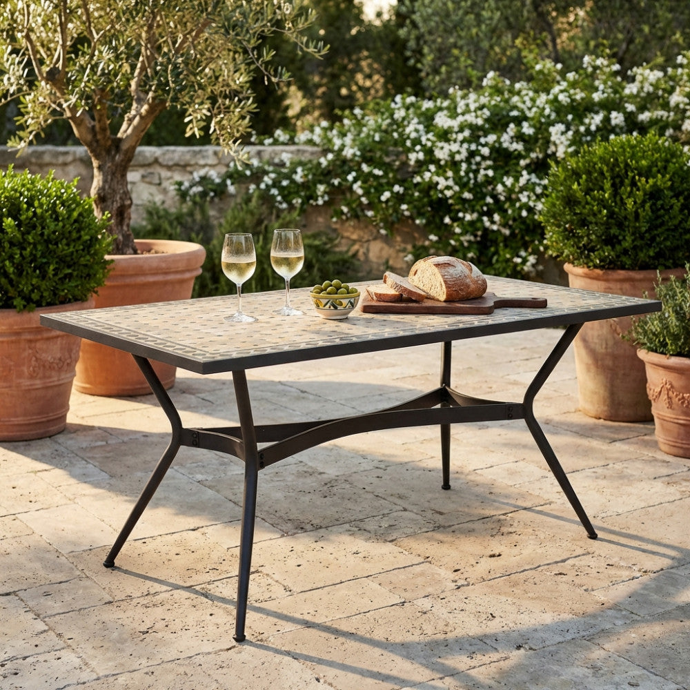 Tavolo vintage in ceramica antracite e beige decorato con vino e pane in un rigoglioso giardino esterno.