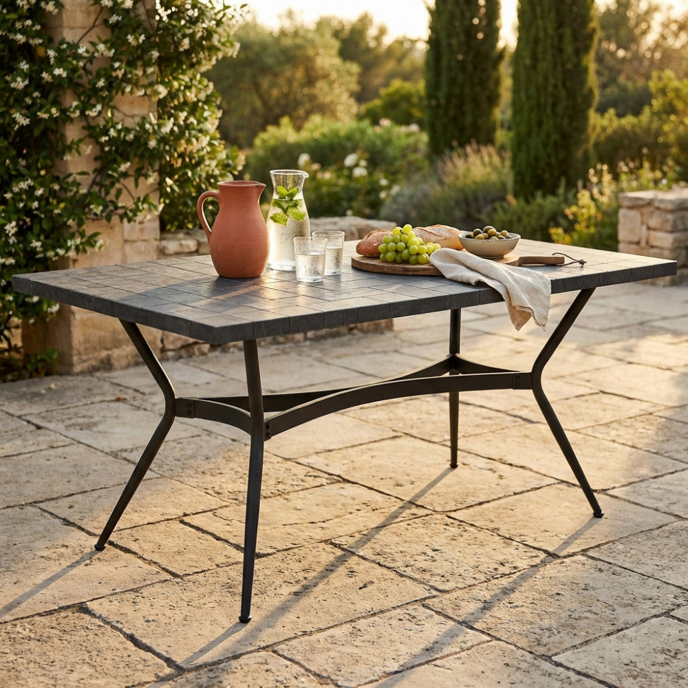 Tavolo da giardino Minosse in ceramica antracite allestito con brocca e frutta su un patio soleggiato.