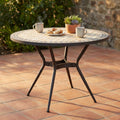 Tavolo da giardino rotondo in ceramica con motivo a mosaico antracite e beige, allestito con caffè su un patio in cotto.