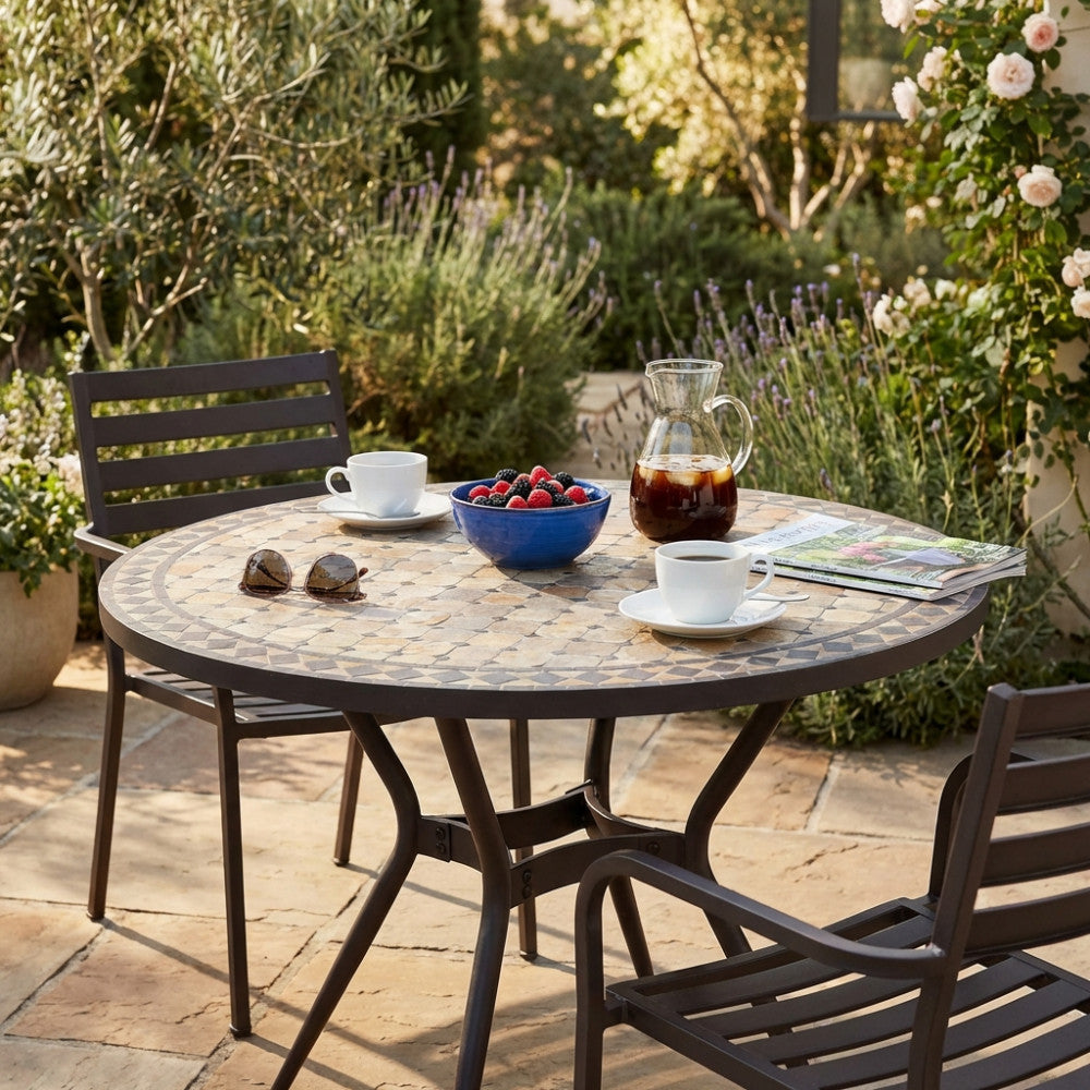 Tavolo da giardino vintage in ceramica con sedute abbinate, decorato con colazione e caffè freddo in un cortile soleggiato.