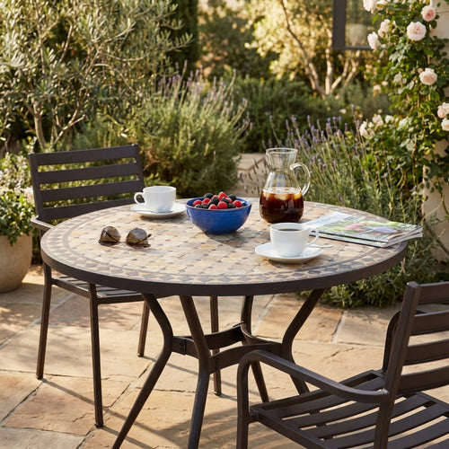 Tavolo da giardino vintage in ceramica con sedute abbinate, decorato con colazione e caffè freddo in un cortile soleggiato.