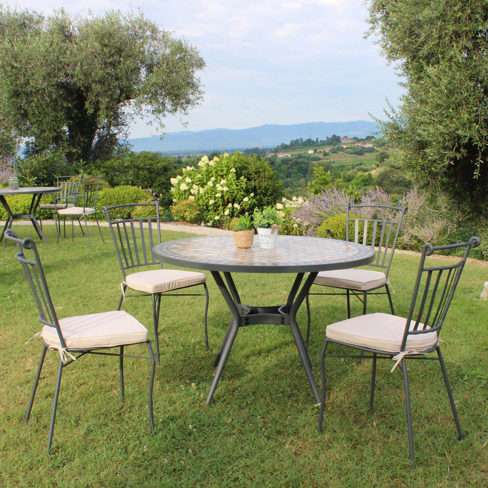 Tavolo da giardino in ceramica con sedie, immerso in un paesaggio collinare verdeggiante.