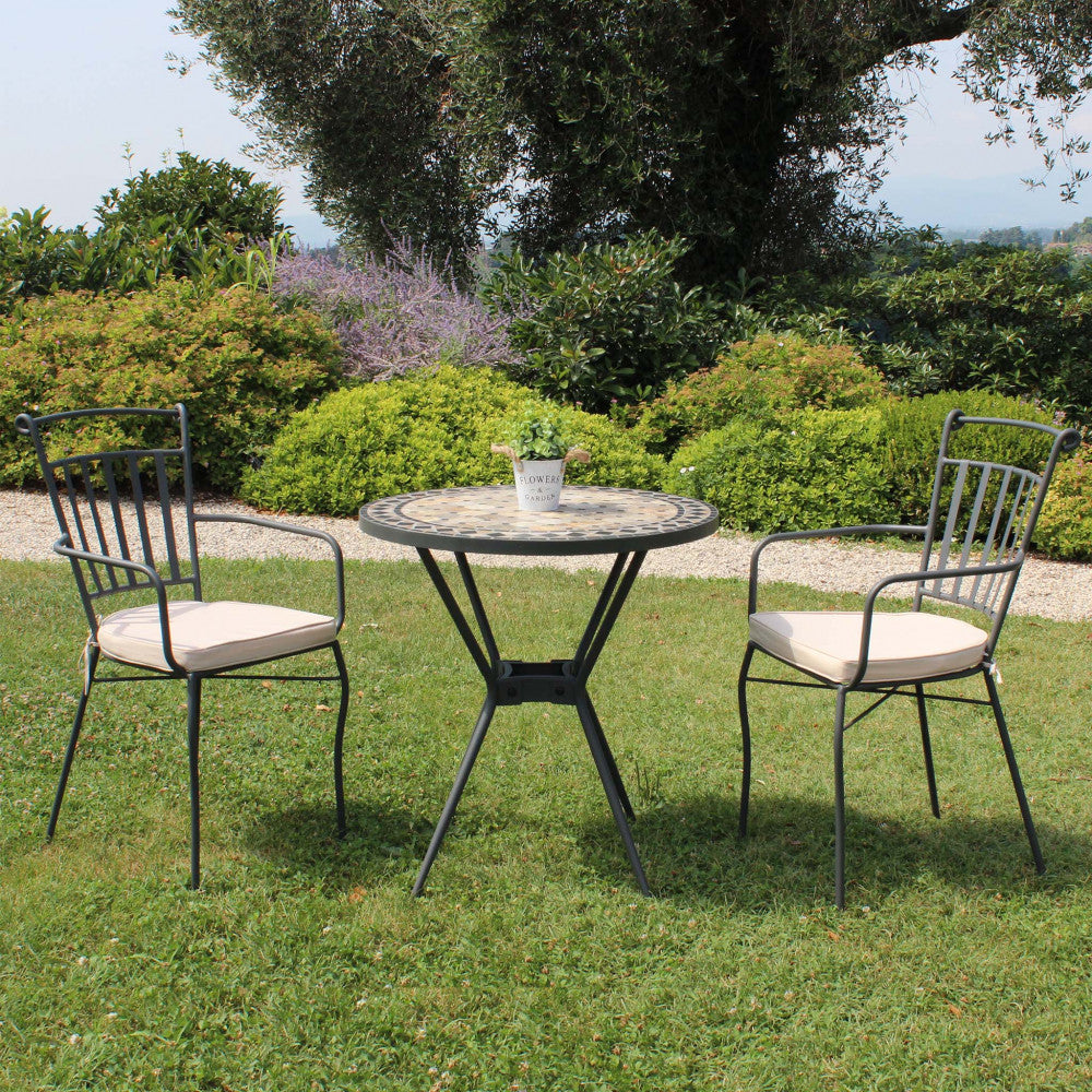 Set da giardino con tavolo rotondo e due sedie in ferro posizionati su prato verde.