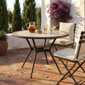 Tavolo da giardino rotondo Prometeo in ceramica allestito su un patio in cotto con bevande fresche.