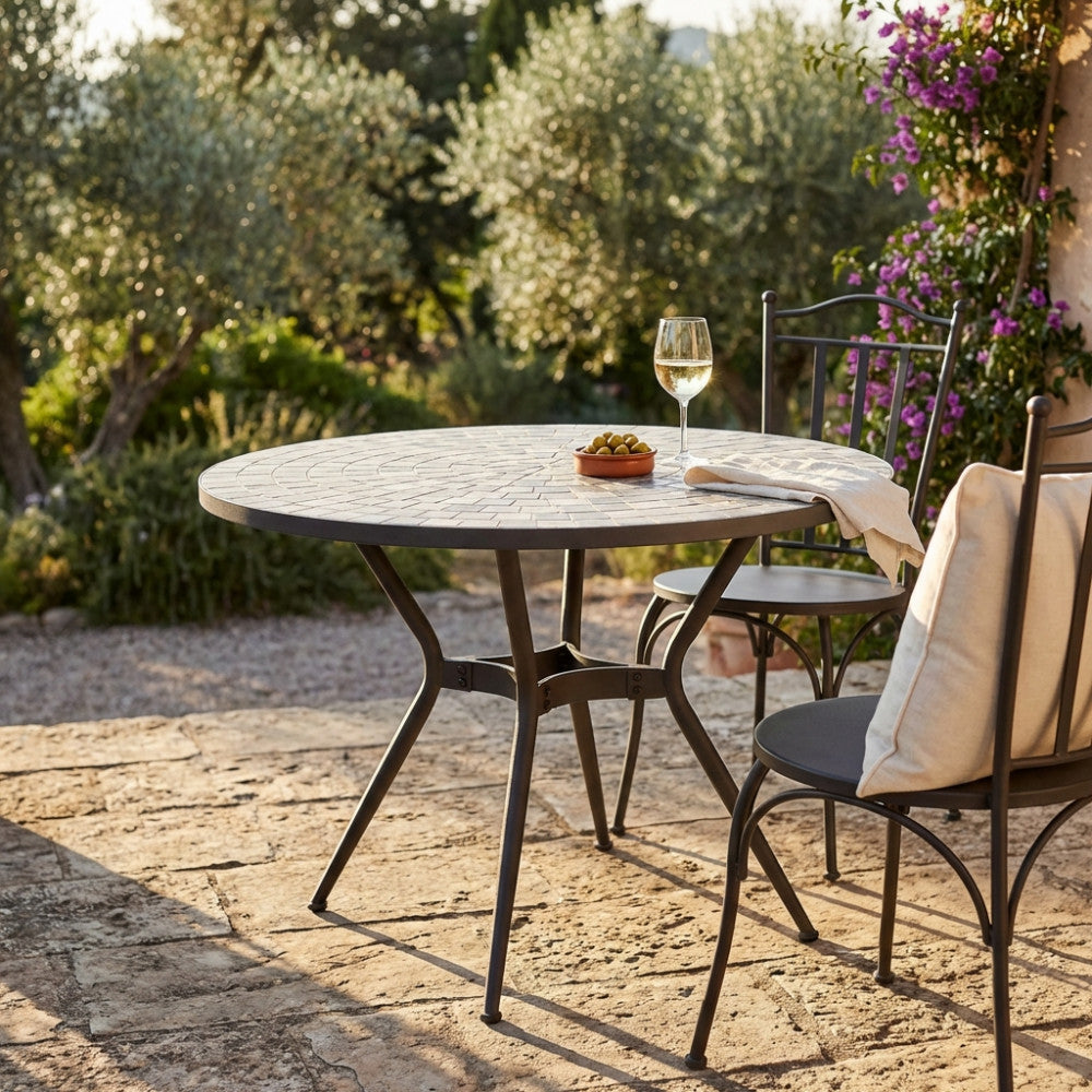 Tavolo da giardino rotondo Zefiro in ceramica antracite e beige allestito in un patio soleggiato.