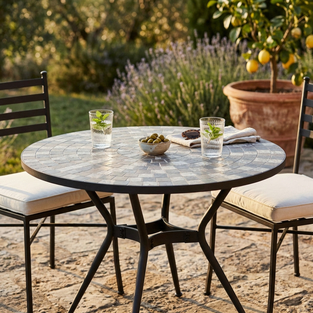 Dettaglio del tavolo Zefiro con due bicchieri e olive, immerso in un rigoglioso giardino mediterraneo.