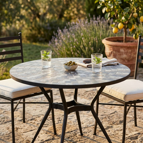 Dettaglio del tavolo Zefiro con due bicchieri e olive, immerso in un rigoglioso giardino mediterraneo.