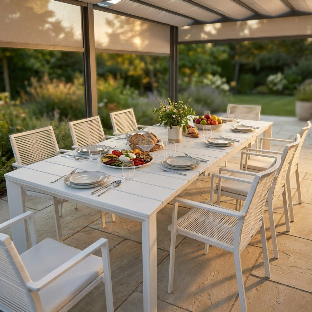 Tavolo da giardino Sacramento in alluminio bianco allestito per un pranzo all'aperto sotto un pergolato.
